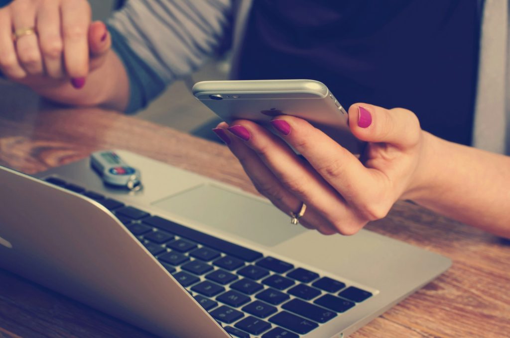 Woman using a phone next to a laptop